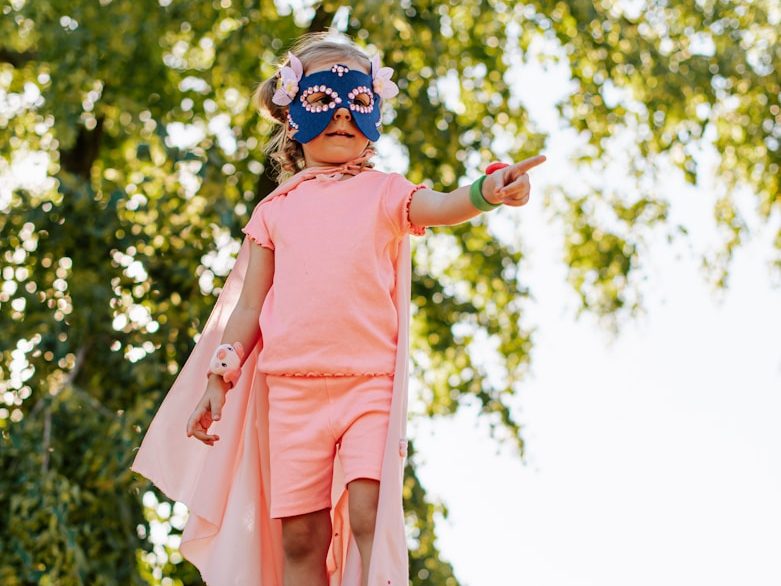 Ein kleines Kind in einem Superhelden-Kostüm zeigt entschlossen auf etwas.