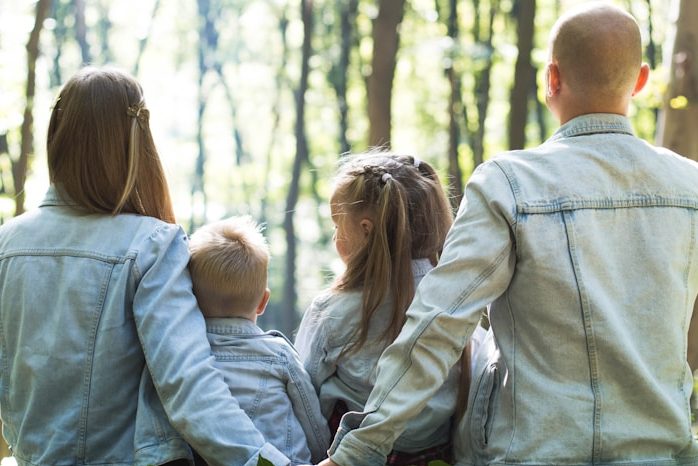 Eine Familie mit zwei Kindern steht nebeneinander im Wald, alle tragen Jeansjacken.