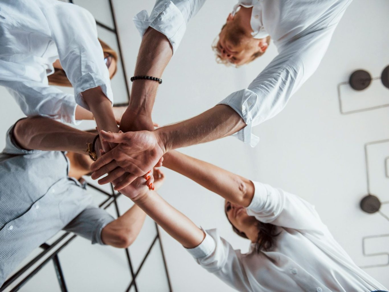 Vier Hände in einem Kreis, die sich aufeinanderlegen, symbolisieren Teamarbeit.