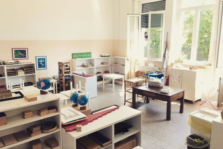 Heller, freundlicher Gruppenraum mit Tischen, Regalen, Spielzeug und Kunstmaterialien.